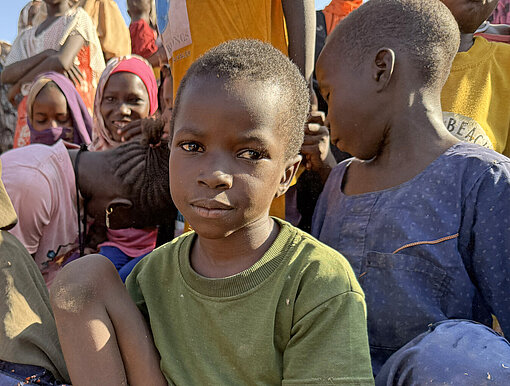 Ein sudanesischer Junge sitzt zwischen anderen Kindern auf dem Boden
