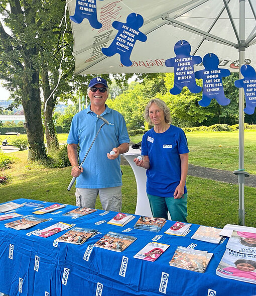 Die Mitglieder der Plan-Aktionsgruppe Essen waren beim Charity-Golfturnier dabei und informierten über das Hilfsprojekt „Ein Platz für Leben“ in Äthiopien Eine Frau und ein Mann stehen an einem Tisch mit Informationsmaterial und dem Logo von Plan International