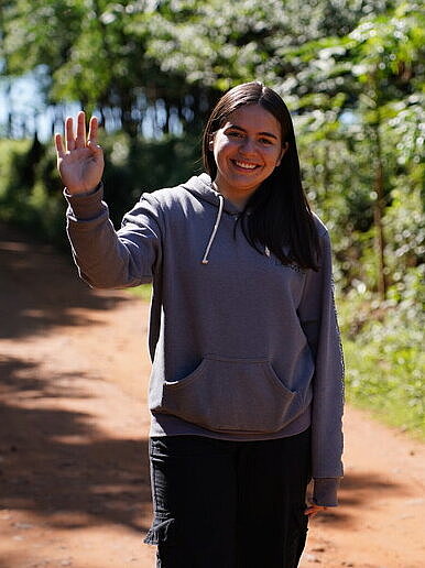 Eine junge Frau steht auf einem Feldweg aus roter Tonerde und winkt