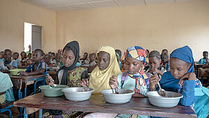 Kinder in Mali sitzen in einem Klassenzimmer und essen gemeinsam aus Schüsseln.