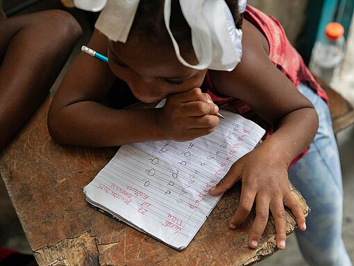 Weil in Haiti neben den Kindern auch die meisten Lehrkräfte auf der Flucht vor exzessiver Gewalt sind, steht das Bildungssystem vor dem Kollaps Ein Kind schreibt in einem Schulheft