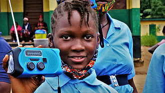 Mädchen aus Sierra Leone hält stolz ein tragbares Radio in die Kamera