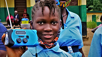 Mädchen aus Sierra Leone hält stolz ein tragbares Radio in die Kamera
