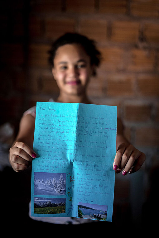 Ein Mädchen hält einen Brief auf blauem Papier in die Kamera.