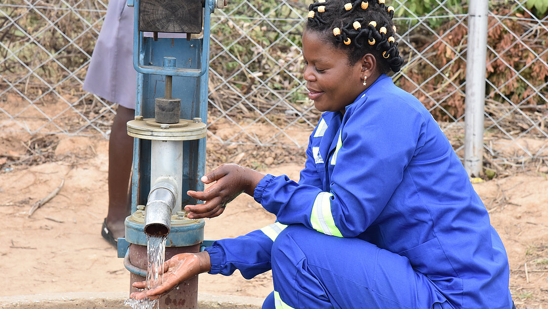 Nomsa kniet vor einer laufenden Wasserpumpe. Nomsa kniet vor einer laufenden Wasserpumpe.