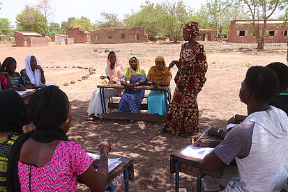 Frauen sitzen in einem Kreis an Schulbänken und sprechen miteinander
