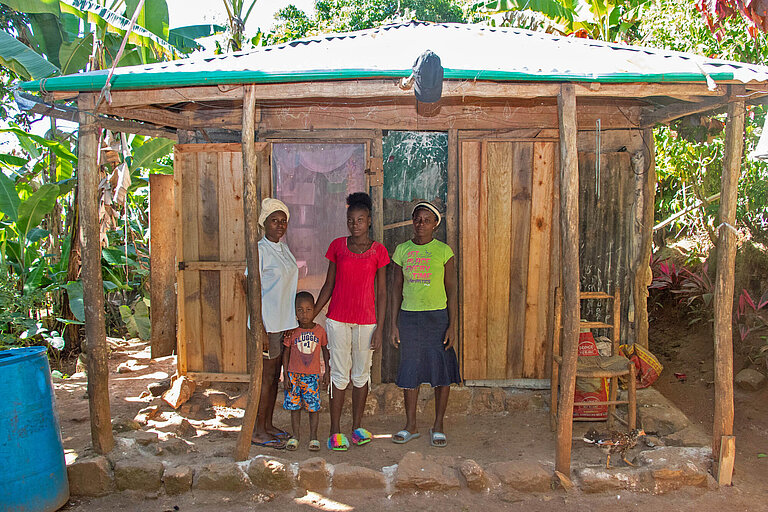 Dina und ihre Familie stehen vor dem Elternhaus in Haiti