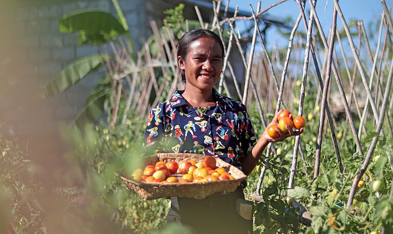 Eine junge Frau steht selbstbewusst auf ihrem Feld zwischen Pflanzen