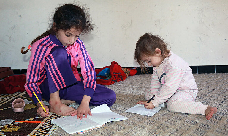Zwei junge Mädchen sitzen auf dem Boden und malen auf Papier