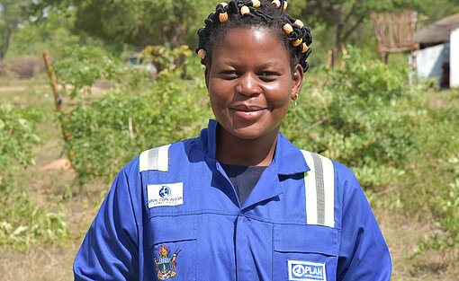 Nomsa sorgt dafür, dass die Schüler:innen an der Schule Zugang zu sauberem, fließenden Wasser haben. Eine Nahaufnahme von Nomsa. Auf ihrem Overall sind die Logos von Plan International und Viva con Agua gestickt.