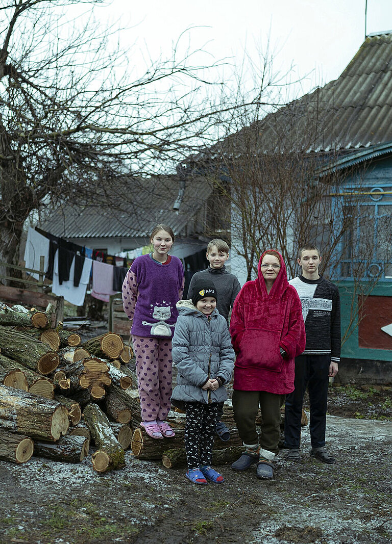 Eine Familie steht draußen vor einem Haus, neben einem großen Haufen Feuerholz