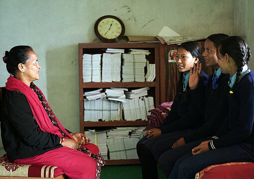 Im Distrikt Kalikot unterstützt Plan International eine schulische Einrichtung für Menstruationshygiene Zwei Mädchen unterhalten sich mit einer Lehrerin im Menstruationsruheraum einer Schule