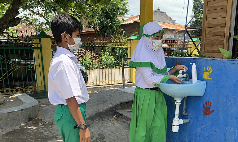 Eine Handwaschanlage im freien, es stehen zwei Kinder an, um sich die Hände zu waschen