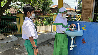 Eine Handwaschanlage im freien, es stehen zwei Kinder an, um sich die Hände zu waschen