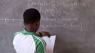 Eine Frau steht vor einer Tafel und schreibt mathematische Formeln.