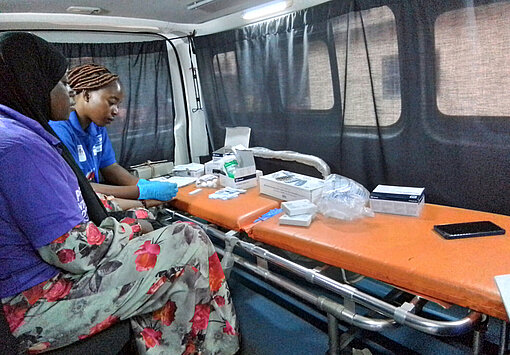 Mabinty (ganz links) macht in Conakry eine Ausbildung zur Schneiderin und lässt sich im rollenden Behandlungszimmer auf HIV testen Eine Frau sitzt im mobilen HIV-Testzentrum