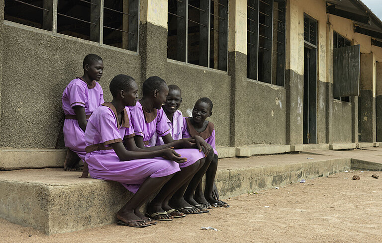 Fünf Mädchen in Schuluniform, darunter Martha, sitzen auf einer Stufe vor dem Schulgebäude und unterhalten sich.