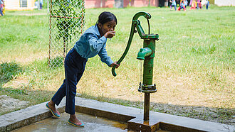 Ein Mädchen trinkt Wasser aus einem Brunnen in Nepal