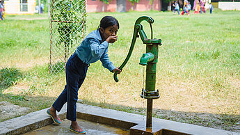 Ein Mädchen trinkt Wasser aus einem Brunnen in Nepal