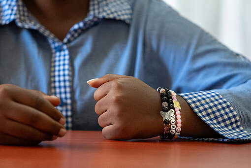 Das Perlenarmband mit der Aufschrift "TRUST" ist für Florence ein stilles Zeichen für Hoffnung und Zusammenhalt Closeup eines Arms mit Perlenarmbänder. Auf einem Armband steht das Wort "Trust".