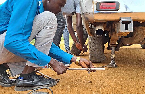 Eine Reifenpanne kann in Südsudan die Gafahr eines Überfalls für die Insassen erhöhen Ein Mann schraubt an einem Reifen