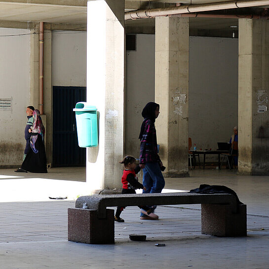 Eine libanesische Jugendliche hat ein Kleinkind an der Hand und läuft mit ihm durch die Notunterkunft