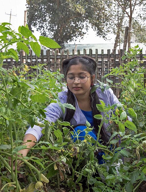 Akhimoni (15) im klimaresistenten Schulgarten eine junge Frau steht in einem Gemüsebeet
