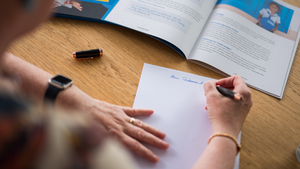Eine Person sitzt beim Testament schreiben für eine Testamentsspende an Plan International an einem Tisch. Sie schreibt auf ein leeres Blatt Papier.