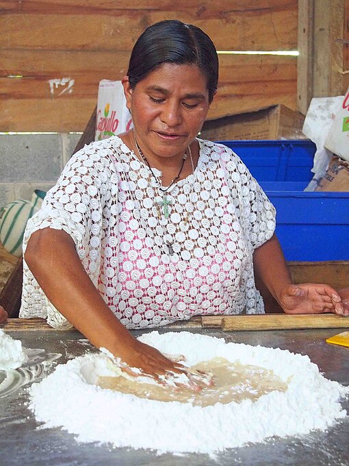Eine Frau in weißer Bluse knetet einen Teig auf einer Tischplatte
