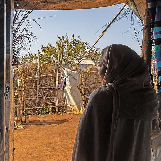 Eine junge Frau blickt aus ihrem Schutzzelt auf einen sandigen Weg