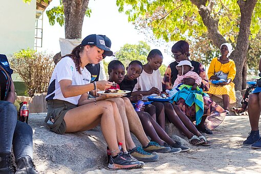 Menschen essen draußen und sitzen auf Steinen