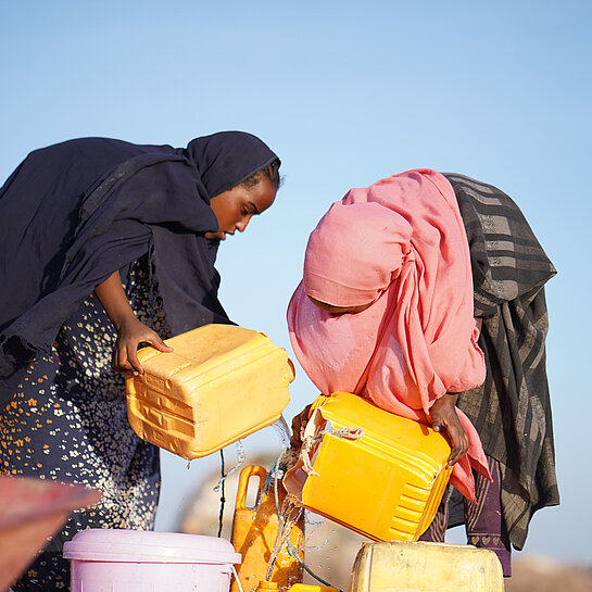 Zwei Mädchen holen Wasser aus einem Brunnen.