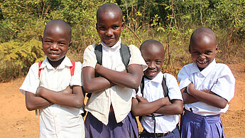 Vier afrikanische Kinder stehen nebeneinander mit verschränkten Armen und schauen verschmitzt in die Kamera.