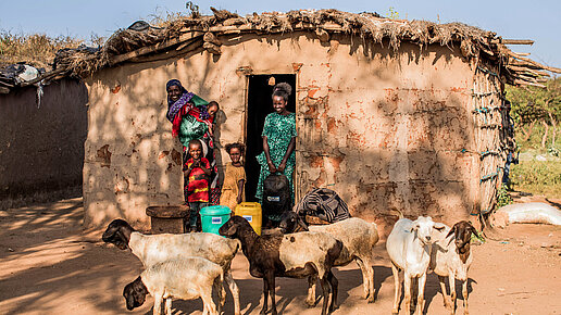 Eine Familie ist mit ihren Ziegen vor ihrem Haus abgebildet.