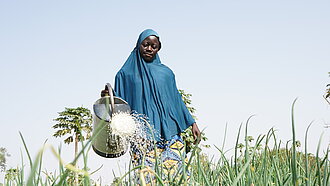 Eine Frau gießt mit einer Gießkanne ein grünes Feld