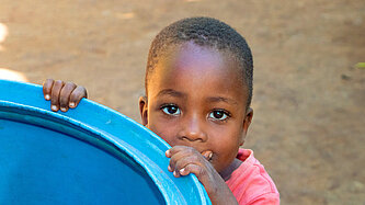 Ein kleiner Junge blickt über den Rand einer Wassertonne