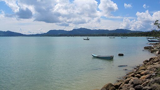 Küste der Andamanensee im Süden Thailamds steiniger Küstenstreifen und Boote im Wasser