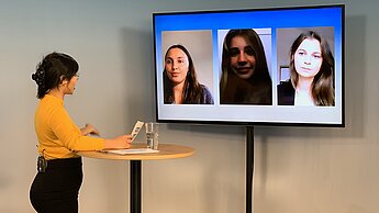 Eine junge Frau steht an einem Pult und ist im Gespräch mit drei Mitgliedern des Plan-Jugendbeirats über einen Bildschirm