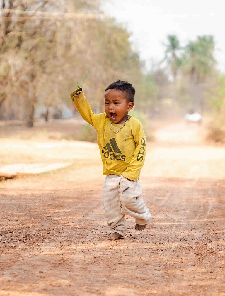 Ein kleiner Junge läuft lachend über einen Sandweg