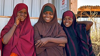 Drei Mädchen in bunten Gewändern stehen lachend nebeneinander