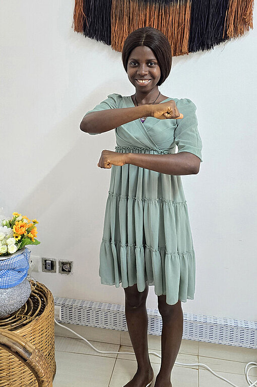 Eine junge Frau in einem grünen Kleid formt ein Gleichheitszeichen mit ihren Armen. Das Zeichen für Gleichberechtigung.