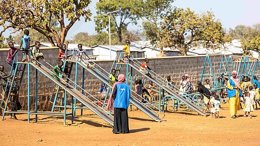 Kinder spielen an einigen nebeneinanderstehenden Rutschen. Plan Mitarbeiterinnen beobachten sie und passen auf. 