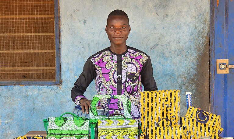 Junger Mann steht vor einem Tisch mit selbstgemachten Gegenständen