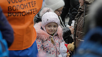 Ein kleines Mädchen mit Stofftier zwischen Menschen