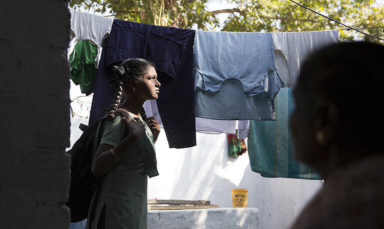 Mädchen steht im Sonnenlicht vor einer Wäscheleine.