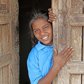 Eine junge Frau in Indien steht lächelnd an einer geöffneten Haustür