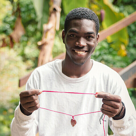 Ein junger Kunsthandwerker hält lächelnd eine handgefertigte Kette vor die Kamera.