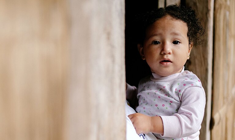 Mayras kleine Tochter blickt aus einem Fenster ihres Zuhauses in der ecuadorianischen Provinz Manabí.