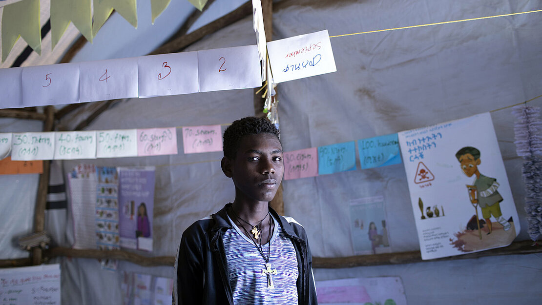 Haftom kam mit seinen Nachbarn in das IDP Camp in Shire. Ein Junge steht in einem Raum und schaut ernst in die Kamera.