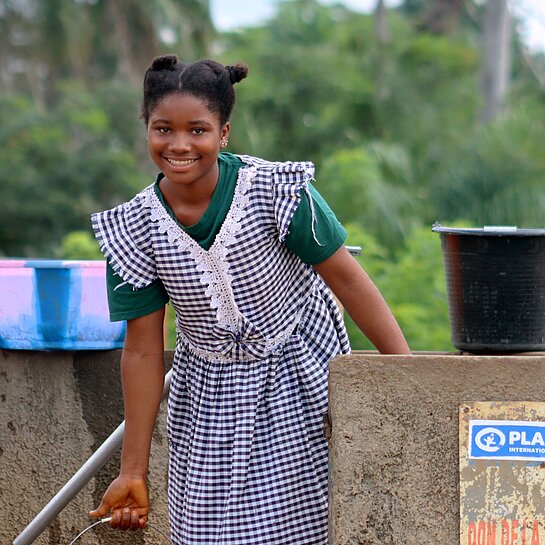Die zwölfjährige Marie-Rose steht mit einem Eimer Wasser am neuen Brunnen auf dem Gelände ihrer Schule in Guinea.